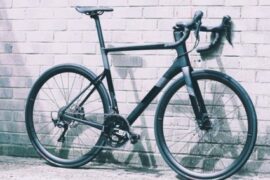 Black Cannondale road bike propped against a white brick wall.