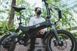 person sat next to a MiRider One Electric Folding Bike in Grey